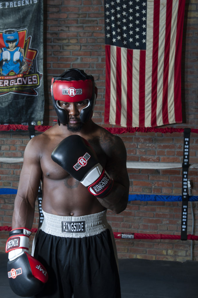 A bxoer with gloves and headgear in the ring in front of US flag