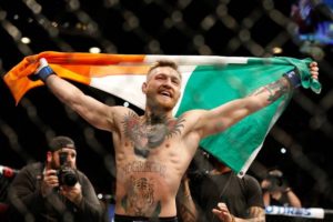 conor mcgregor holding up the Irish flag after a win in the octagon