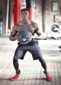 agility training for boxing - athlete doing side step with resistance bands at ankle and holding medicine ball