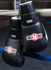 Best boxing gloves: black quick-tie training gloves hanging from the ring ropes.