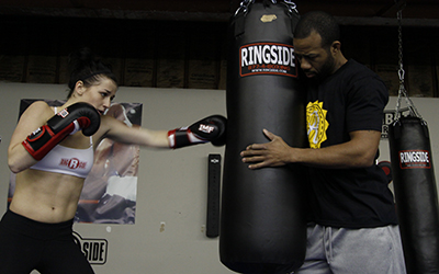 A fighter hits the heavy bag while her coach offers feedback.