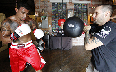 coach braces punch shield against forearm while boxer with white gloves prepares to strike with a hook.