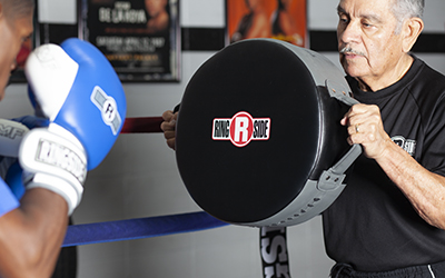 coach holds punch shield for boxer in blue gloves