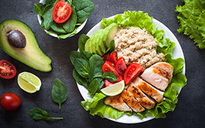 A plate with grilled chicken, quinoa, sliced avocado, raw spinach, and quartered tomatoes.