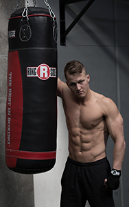 Fit boxer with no shirt stands next to a heavy bag.