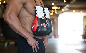 A fit boxer stands in the gym with a pair of gloves draped around his neck.